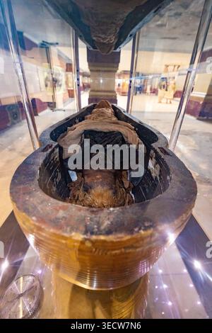 MUSÉE ÉGYPTIEN, LE CAIRE, ÉGYPTE - 25 MAI 2025 : une ancienne momie égyptienne couchée à l'intérieur d'un sarcophage ouvert en bois sombre, exposée sous verre dans un galler Banque D'Images