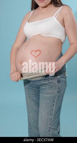 Ventre de femme enceinte avec un coeur rouge se rapprochant Banque D'Images
