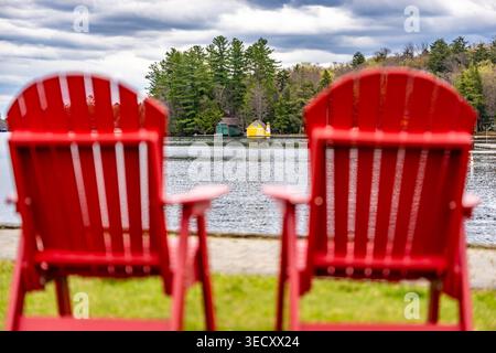 Old Forge, NY, USA - 29 avril 2026 deux chaises Adirondack rouge vif sont assises vides sur une pelouse verte luxuriante, offrant une vue paisible. Banque D'Images