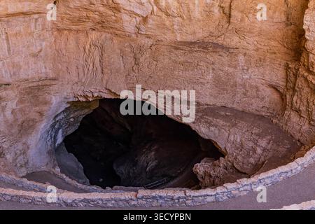 Une grande ouverture sombre dans une paroi rocheuse accidentée de couleur claire révèle l'intérieur d'un système de grottes. Banque D'Images