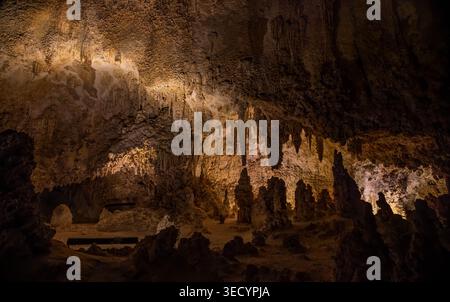 De magnifiques piliers de calcaire et des stalactites texturées se dressent dans une chambre souterraine faiblement éclairée éclairée par des lumières artificielles chaudes. Banque D'Images