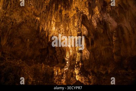 Des formations de calcaire orange illuminées, y compris des stalactites et des piliers, émergent de l'ombre dans un environnement mystérieux de caverne souterraine. Banque D'Images