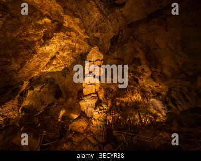 Les stalagmites illuminées et les formations rocheuses coulantes se dressent dans la lueur ambre chaude d'une caverne souterraine. Banque D'Images