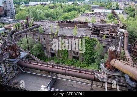 Vue sur un bâtiment industriel abandonné avec de grands pipelines et une végétation envahissante à l'usine sidérurgique de Völklingen, Sarre, Allemagne. Banque D'Images