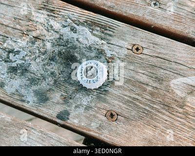 Riga, Lettonie - 30 avril 2026 : gros plan d'un bouchon de bouteille mis au rebut sur un banc en bois usé avec de la peinture pelable et des vis rouillées. Détail urbain highlighti Banque D'Images