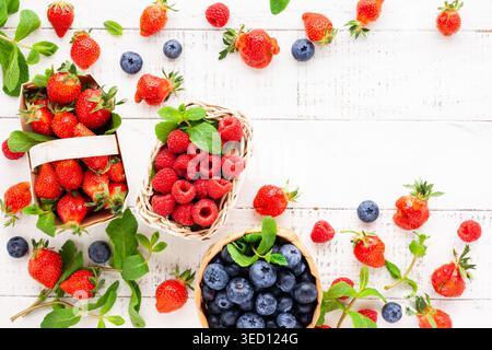 Différentes baies fraîches dans un panier sur fond de bois blanc, vue de dessus.Concept de la cuisine d'été.Flat lay, espace de copie. Banque D'Images