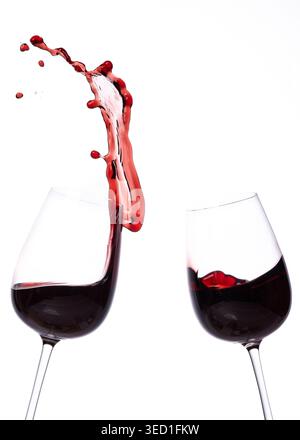Le vin rouge se déverse entre deux verres sur une surface blanche Banque D'Images