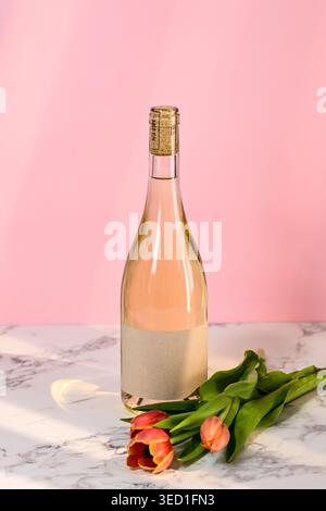 Bouteille de vin rosé se tient à côté de tulipes fraîches sur marbre. Banque D'Images