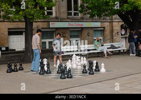 Les gens jouent sur des échiquiers géants en plein air dans les jardins Victoria devant la bibliothèque centrale de Leeds et le PINC College, Leeds, West Yorkshire, Royaume-Uni Banque D'Images