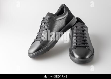 Baskets basses masculines tendance en cuir noir à la mode avec lacets et semelle en caoutchouc sur fond gris neutre. Style décontracté. Paire de chaussures pour homme. Banque D'Images
