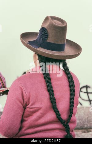 Vue arrière d'une femme andine locale portant un chapeau traditionnel à large bord et de longs cheveux tressés à l'extérieur du marché San Pedro à Cusco, au Pérou. Banque D'Images