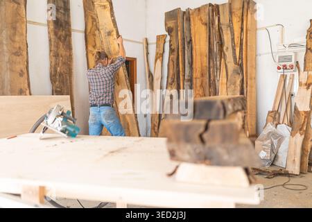 Charpentier déplaçant manuellement la dalle de bois brut à l'intérieur de l'atelier Banque D'Images