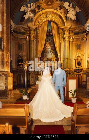 Couple se tient devant l'autel pendant la cérémonie de mariage dans l'église. couple fait face à l'autel dans l'église. Ils portent une tenue de mariage. caractéristiques intérieures ornées de Banque D'Images