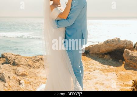 Couple célèbre mariage par l'océan au coucher du soleil avec des vagues en arrière-plan. couple se tient ensemble sur la rive rocheuse profitant du jour du mariage. le soleil se couche sur le Banque D'Images
