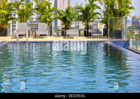 Phnom Penh, Cambodge - 14 janvier 2024 : piscine à débordement sur le toit de Phnom Penh avec horizon de la ville et palmiers en pot sous un ciel bleu clair. Banque D'Images