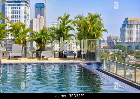 Phnom Penh, Cambodge - 14 janvier 2024 : piscine à débordement sur le toit de Phnom Penh avec horizon de la ville et palmiers en pot sous un ciel bleu clair. Banque D'Images