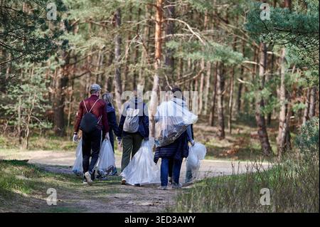 Groupe de quatre volontaires marchant le long du rivage transportant des sacs en plastique de déchets collectés, Gdansk, Poméranie, Pologne, Europe. Banque D'Images