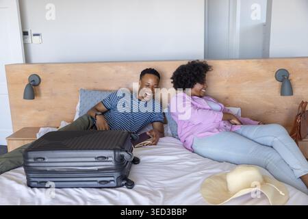 Couple afro-américain s'inclinant dans la chambre dans des vêtements décontractés, tenant le passeport près de la valise et du chapeau Banque D'Images