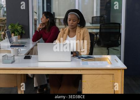 Diverses collègues féminines travaillant au bureau, en blazer brun et pull marron à l'aide d'ordinateurs portables Banque D'Images