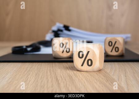 Cubes en bois avec des signes de pourcentage sur un bureau. Presse-papiers floue avec des documents professionnels et une loupe en arrière-plan. Concept pour financier i Banque D'Images