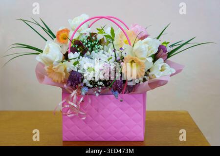 Arrangement floral lumineux dans un panier rose avec diverses fleurs sur une table Banque D'Images