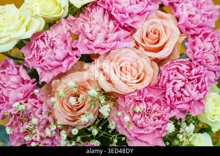 Un groupe de roses roses et d'œillets sont disposés avec des fleurs blanches dans une boutique de fleurs. La verdure entoure les fleurs ajoutant à leur beauté. Banque D'Images