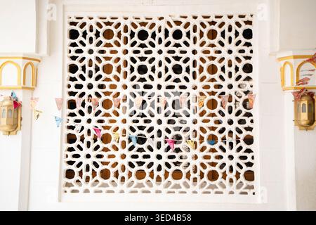 Moustiquaire décorative mashrabiya avec motif arabesque géométrique et drapeaux suspendus colorés sur la façade murale blanche. Architecture islamique, tra Banque D'Images