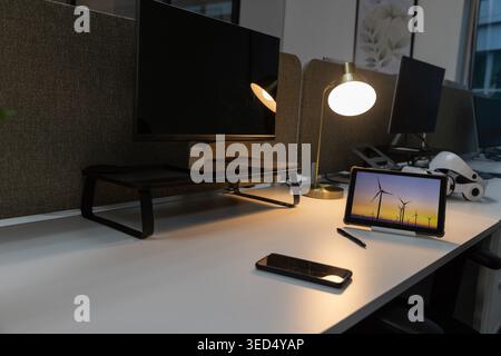 Tablette sur le stand affiche des éoliennes au coucher du soleil sur le bureau blanc, lampe en laiton brillante Banque D'Images