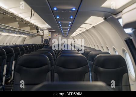 Un intérieur de cabine d'avion commercial complètement vide présente de longues rangées de sièges passagers avec des plafonniers éclairés le long de l'allée centrale. Banque D'Images