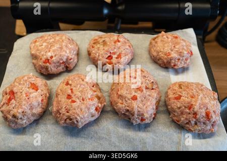 Galettes maison crues avec paprika sur un gril de contact en utilisant du papier parchemin pour garder la surface propre, astucieux sac de sauvetage de cuisine pour une cuisson facile. Banque D'Images