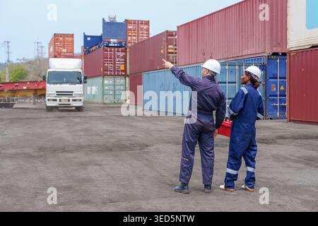 Homme caucasien mi-adulte et femme noire en équipement de sécurité avec boîte à outils coordonner la cargaison à un terminal. Idéal pour la chaîne d'approvisionnement, la logistique et le shi global Banque D'Images