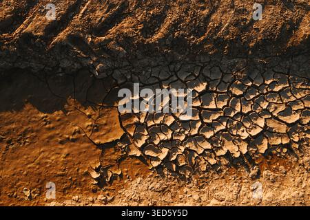 Vue de dessus de boue fissurée et de terre sèche révélant les textures de lit de rivière stressées par la sécheresse au coucher du soleil, directement au-dessus Banque D'Images