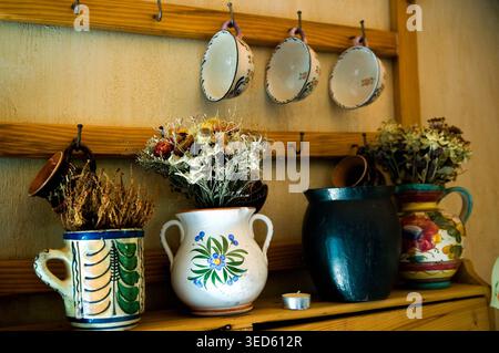 Tasses à thé suspendues dans une rangée. Les cruches et la tasse avec des bouquets séchés se tiennent sur une étagère Banque D'Images