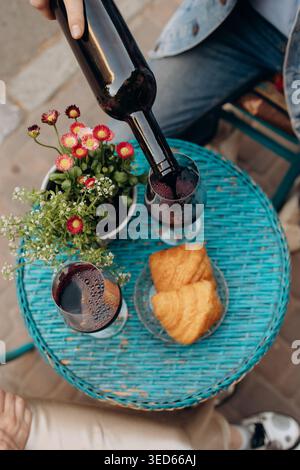 Verser du vin rouge dans des verres pendant le petit déjeuner extérieur avec des croissants Banque D'Images