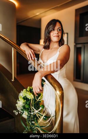 Mariée élégante tenant le bouquet sur l'escalier dans la lumière intérieure chaude Banque D'Images