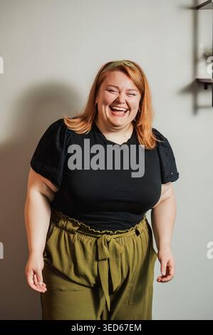 Femme riant en haut noir et pantalon olive près de l'étagère murale Banque D'Images