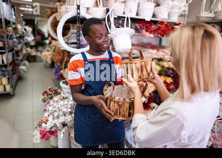 Fleuriste montrant différents paniers en bois à un client dans un magasin de fleurs, l'aidant à choisir le bon Banque D'Images