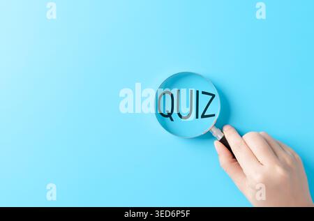 Test de quiz concept d'apprentissage et d'évaluation de l'éducation. main tenant la loupe sur le texte du quiz sur fond bleu, symbolisant la vérification des connaissances, Banque D'Images