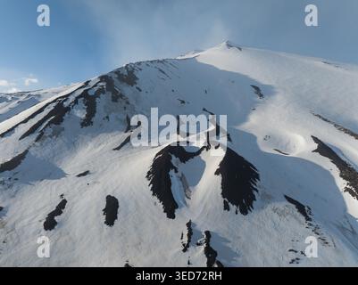 Vue aérienne du versant sud enneigé de l'Etna avec des cratères volcaniques et des plaques de lave sombres sous un ciel bleu clair à Nicolosi, Sicile Banque D'Images