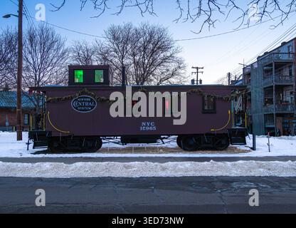 Ypsilanti, États-Unis - 12 février 2026 : wagon de caboose vintage décoré avec guirlande de vacances, garé à côté de la rue enneigée au crépuscule ; arbres sans feuilles, puissance l Banque D'Images