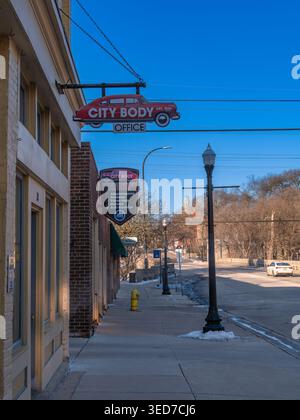 Ypsilanti, États-Unis - 12 février 2026 : rue calme de petite ville avec vitrines et panneau suspendu vintage pour magasin d'automobiles de carrosserie de ville, ciel bleu clair, hiver l Banque D'Images