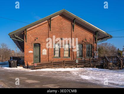 Ypsilanti, États-Unis - 12 février 2026 : bâtiment historique de dépôt en briques rouges avec toit à pignon, neige d'hiver, ciel bleu, rampe en bois et garde-corps, petite ville str Banque D'Images