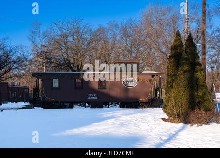 Ypsilanti, États-Unis - 12 février 2026 : caboose de chemin de fer brun vintage dans un parc enneigé avec des arbres sans feuilles, ciel bleu et feuilles persistantes, la journée en hiver Banque D'Images