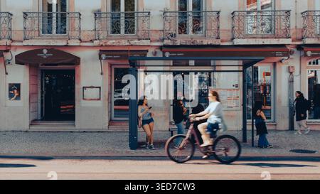 Lisbonne, Portugal - 15 mai 2025 : Womman fait du vélo devant d'autres qui attendent à un arrêt de bus dans la ville animée de Lisbonne Banque D'Images