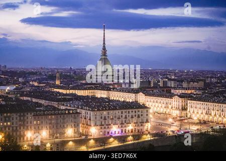 Vue aérienne de la mole Antonelliana et la ligne d'horizon illuminée de la ville avec les Alpes en arrière-plan au crépuscule à Turin, Piémont, Italie. Banque D'Images