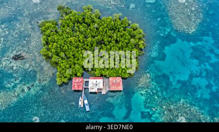 Vue aérienne de bateaux amarrés par des bâtiments en bois sur une île tropicale, Tumbak Bentenan Marine Park, Minahasa, Sulawesi du Nord, Indonésie Banque D'Images