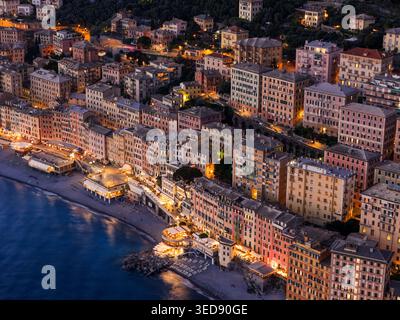 Vue aérienne des façades colorées illuminées de la ville côtière historique le long de la plage de galets au crépuscule Camogli, Ligurie, Italie. Banque D'Images
