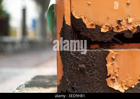 Cette photographie en gros plan capture un mur altéré avec une peinture orange écaillée et une base noire et corrodée, mettant en évidence les textures de la décomposition et de l'extérieur Banque D'Images
