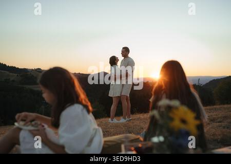Famille avec enfants pique-nique dans la nature, coucher de soleil. Vue arrière. Banque D'Images