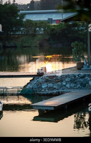 Une scène de soirée sereine représentant un lac tranquille au coucher du soleil, avec de doux reflets sur l'eau et un quai rustique invitant des moments paisibles dans la nature Banque D'Images